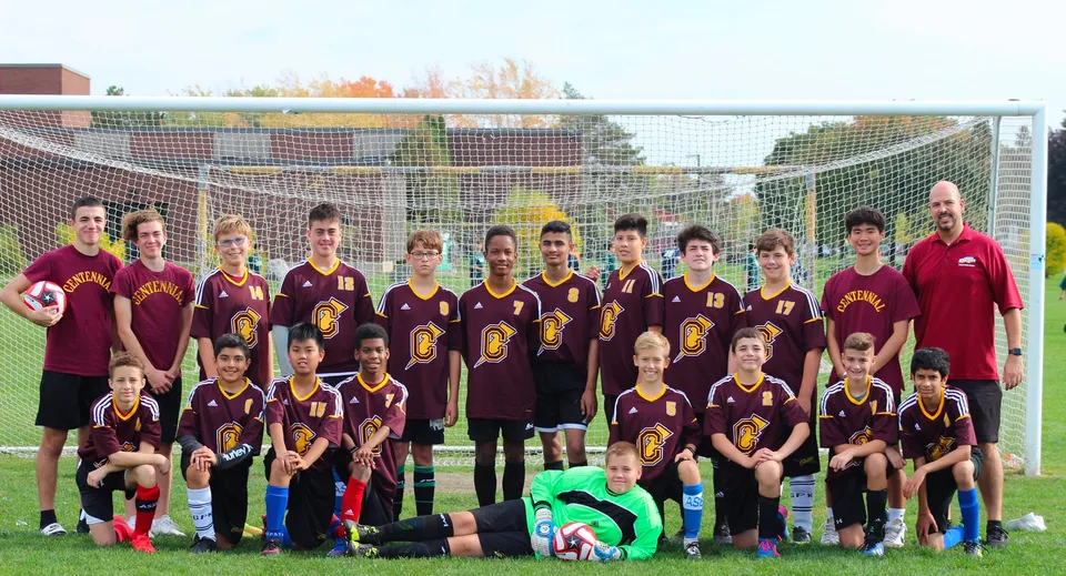 Un gruppo di studenti e studentesse della Centennial Regional High School posa insieme su un campo da calcio con lo skyline della città sullo sfondo.