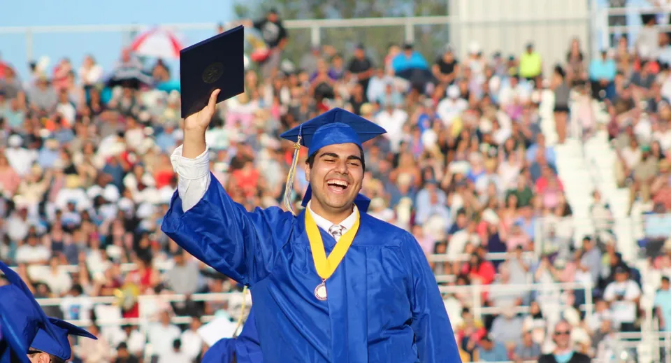 Un neodiplomato con tocco e toga blu si trova davanti a una folla durante la cerimonia di diploma del Placentia-Yorba Linda Unified School District.