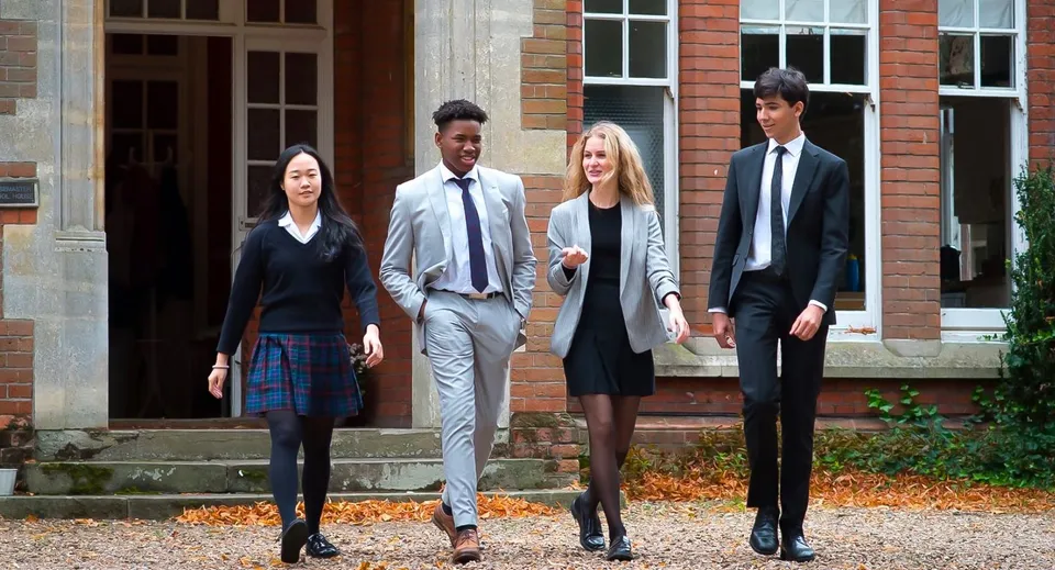 Quattro persone ben vestite si trovano sui gradini di un edificio in mattoni nel campus della Woodbridge School in autunno.