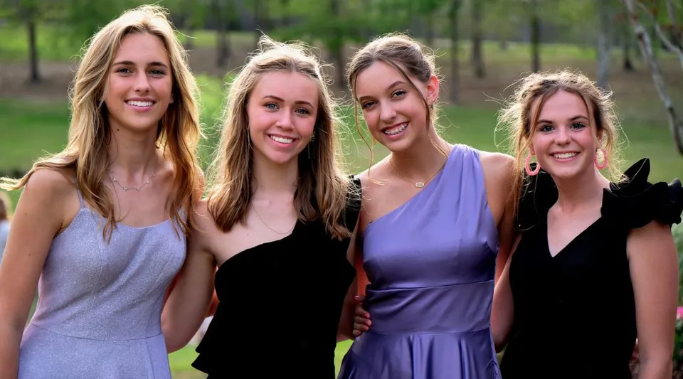 Quattro studentesse sorridono su un prato con alberi nel campus della Bayshore Christian School.