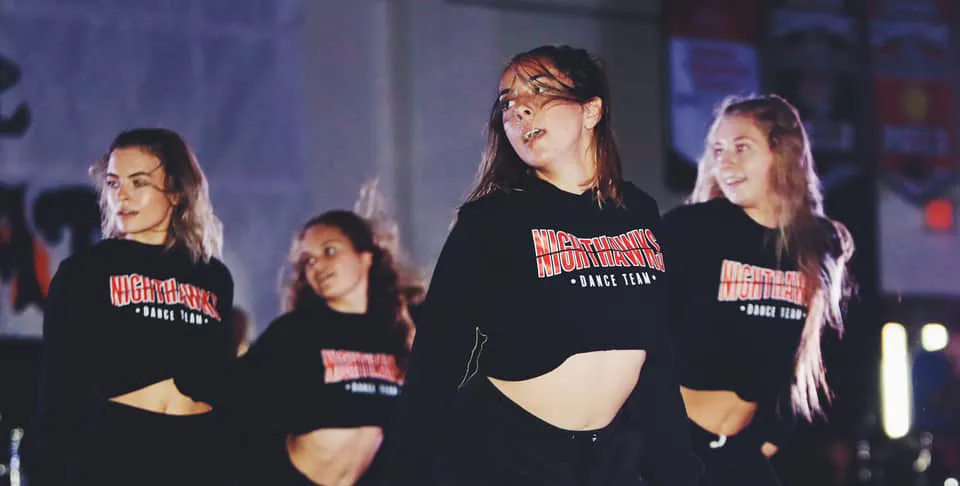 Un gruppo di studentesse della Murietta Valley High School indossa felpe con cappuccio nere con un logo speciale in una stanza poco illuminata.