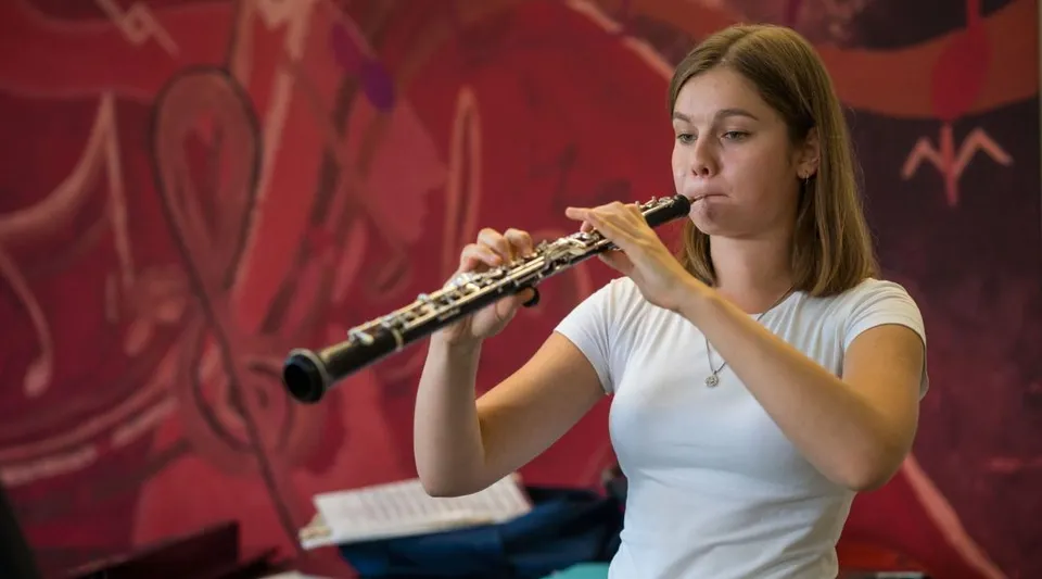 Una studentessa della The Purcell School for Young Musicians suona il flauto su un palco con sfondo rosso.
