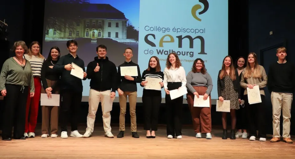 Un gruppo di studenti e studentesse della Episcopal Sem' De Walbourg si trova sul palco e tiene in mano dei certificati.
