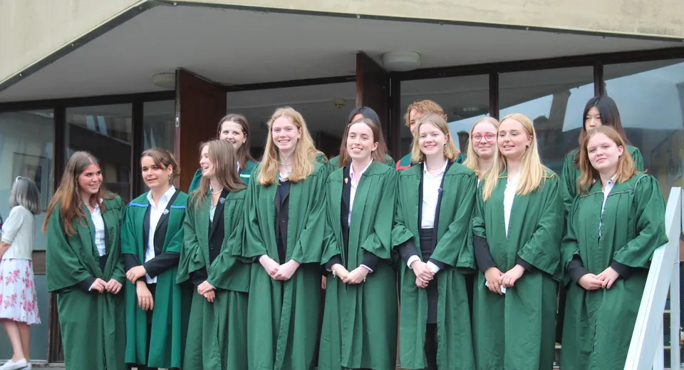 Un gruppo di giovani diplomate della Leweston School posa in toga verde da cerimonia davanti a un edificio con un passaggio coperto.