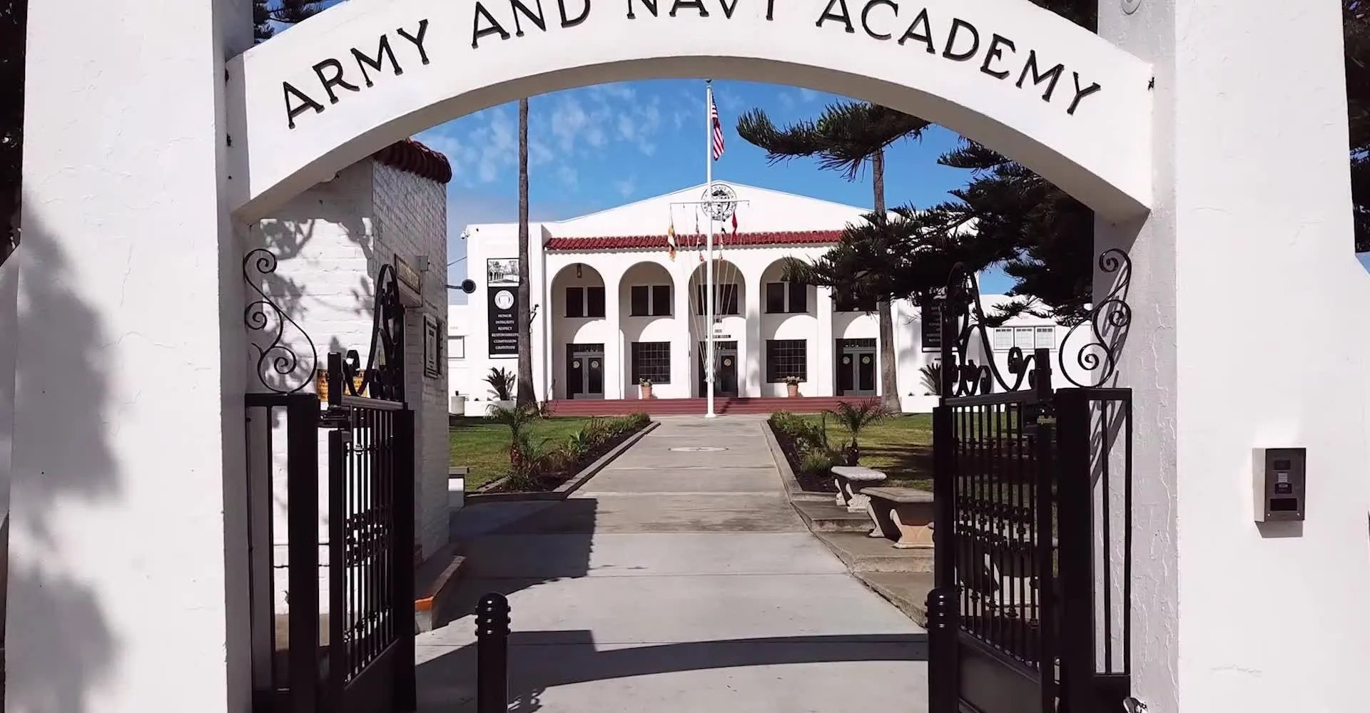 L'arco bianco d'ingresso della Army and Navy Academy mostra l'edificio principale con palme e un pennone con la bandiera.