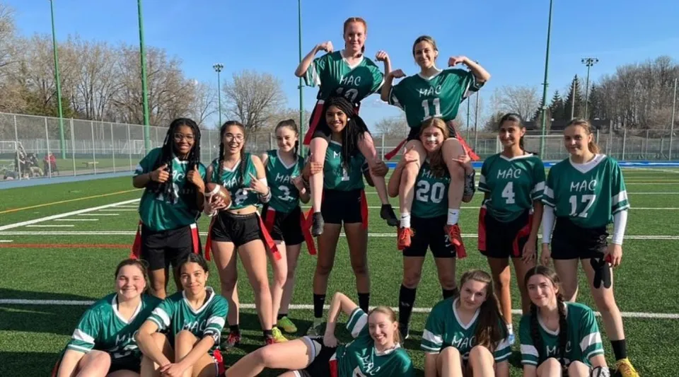 Un gruppo di giovani atlete con maglie verdi e nere posa su un campo da gioco della Macdonald High School.