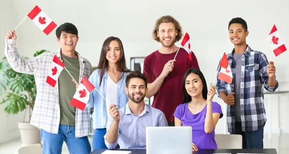 Grupo de jóvenes de diversas etnias sonriendo y sosteniendo pequeñas banderas de Canadá