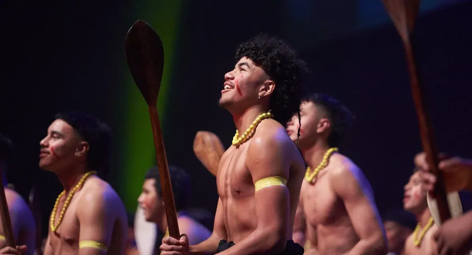 Gli studenti del Rongotai College eseguono una performance di danza tradizionale con pagaie e accessori gialli su un palco.