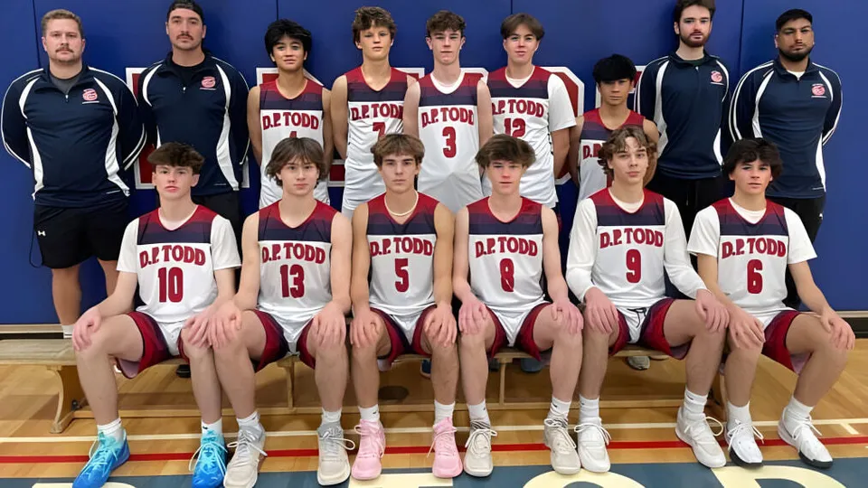 Un gruppo di giovani giocatori di pallacanestro posa insieme nella palestra della D.P. Todd Secondary School.