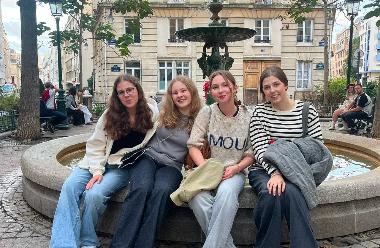 Quattro studentesse sedute sul bordo di una fontana in una piazza di Parigi