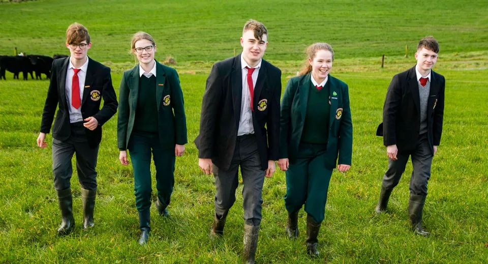 Studenti della Royal School Cavan si trovano su un campo erboso con mucche sullo sfondo.