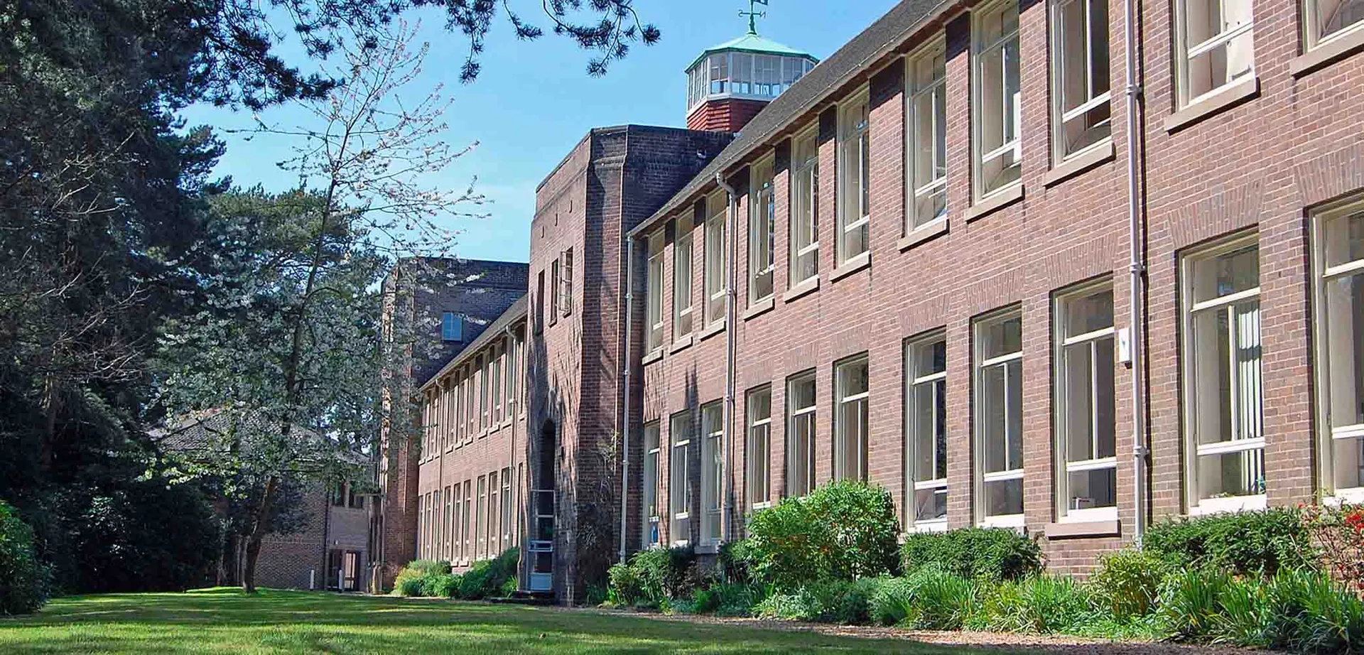L'edificio in mattoni a più piani con tetto verde della Talbot Heath School è circondato da alberi e curati spazi verdi.