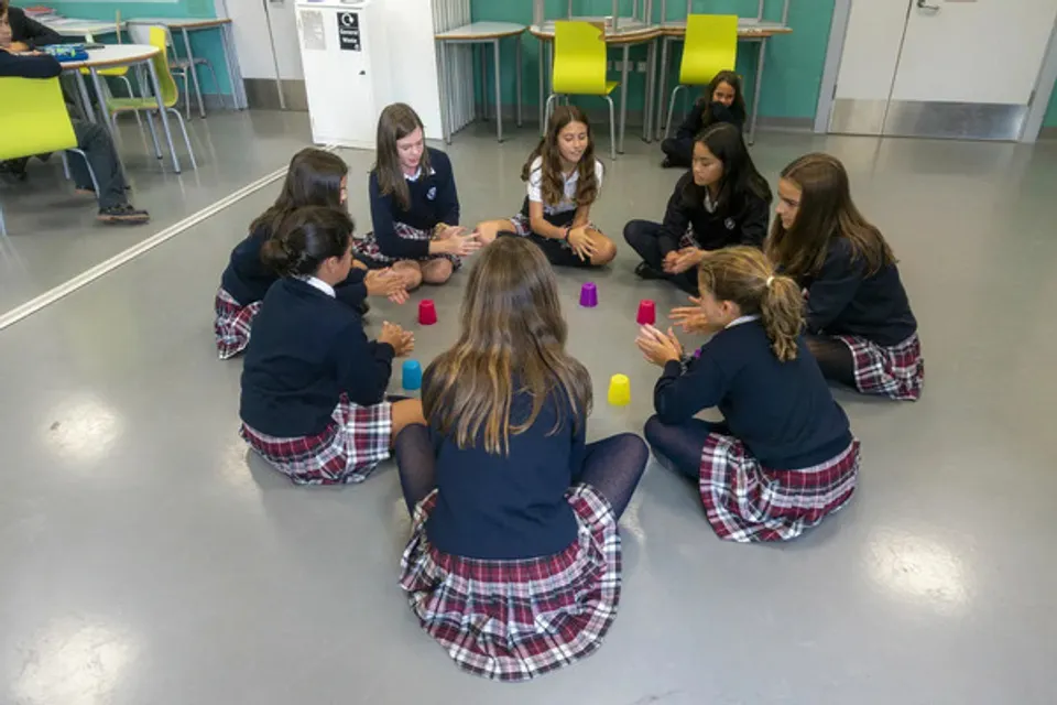 Studentesse della SEK International School Dublin siedono in cerchio sul pavimento, con bicchieri colorati davanti.