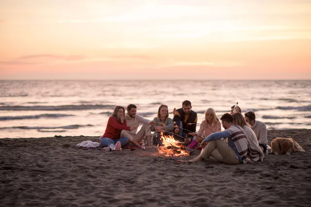 Grupo de amigos sentados alrededor de una hoguera en la playa al atardecer