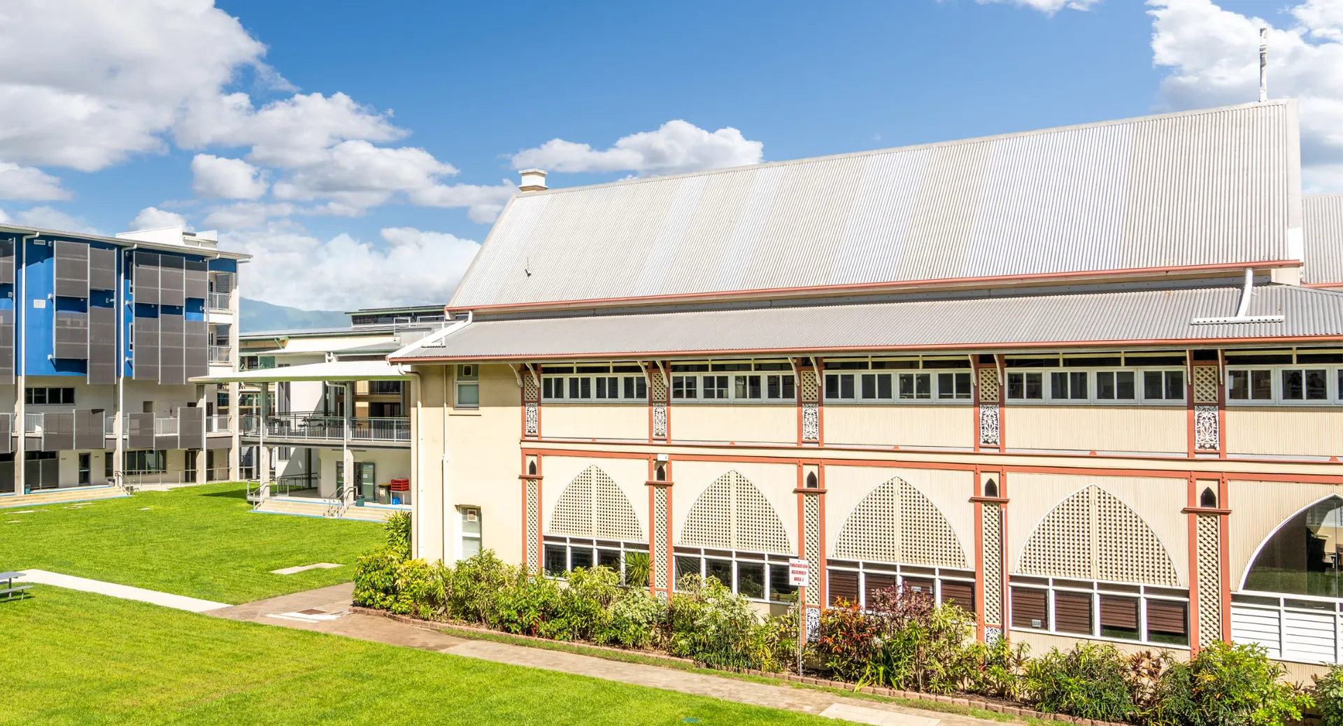 L'edificio moderno a più piani della Christ King Secondary School è circondato da un verde lussureggiante sotto un cielo blu con nuvole.