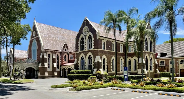 Il prestigioso edificio in mattoni con torre e finestre ad arco nel campus del Fraser Coast Anglican College è circondato da palme.