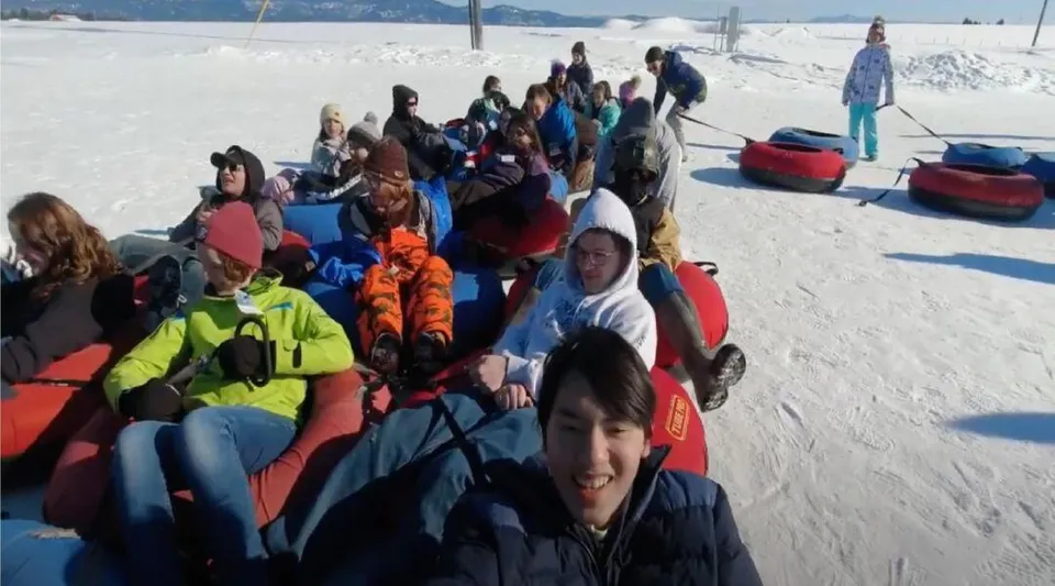 Un gruppo di studenti della Huntington High School è riunito in abbigliamento invernale su un pendio innevato con uno skilift sullo sfondo.