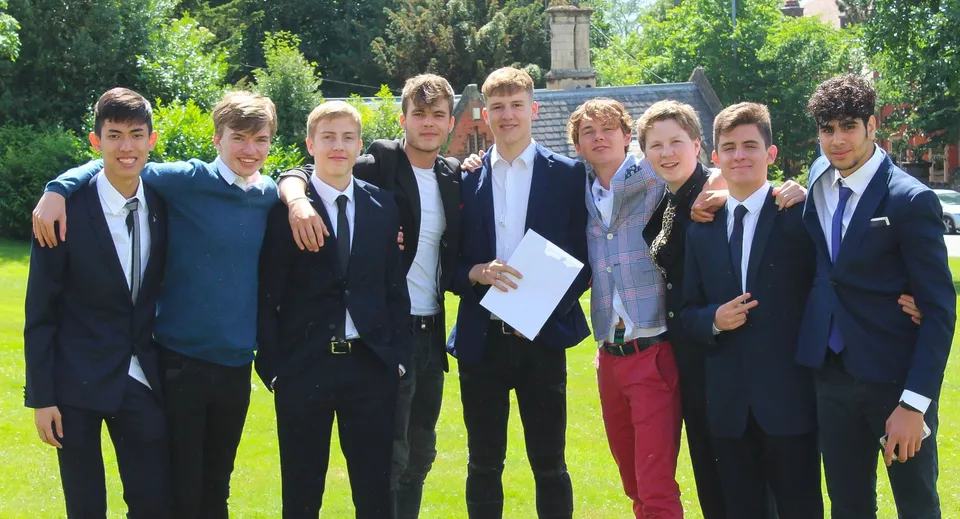 Un gruppo di studenti della Royal School Wolverhampton posa in abito formale nel verde davanti a un monumento.