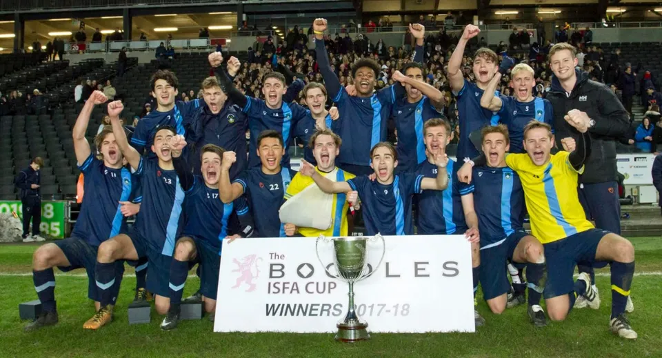 La squadra di calcio del Bradfield College festeggia nello stadio con una coppa in mano.
