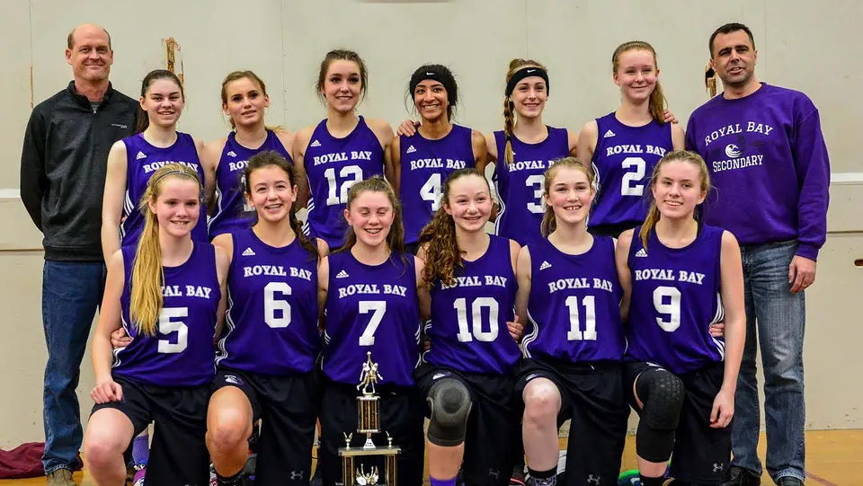 La squadra di basket della Royal Bay Secondary School si trova insieme in una stanza con un trofeo in primo piano.