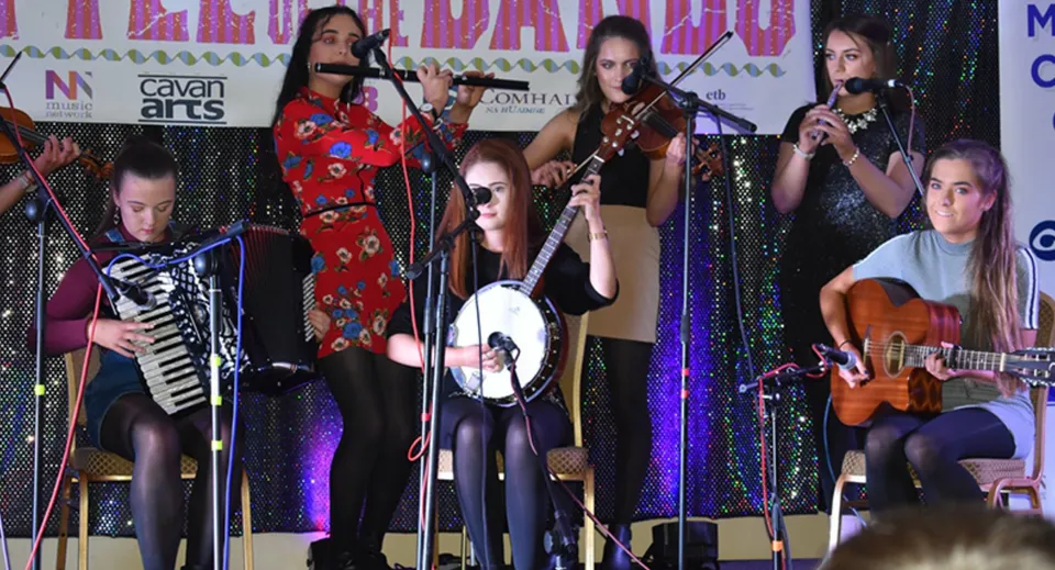 Un gruppo di musiciste e musicisti del Loreto College Cavan si esibisce sul palco sotto luci colorate.