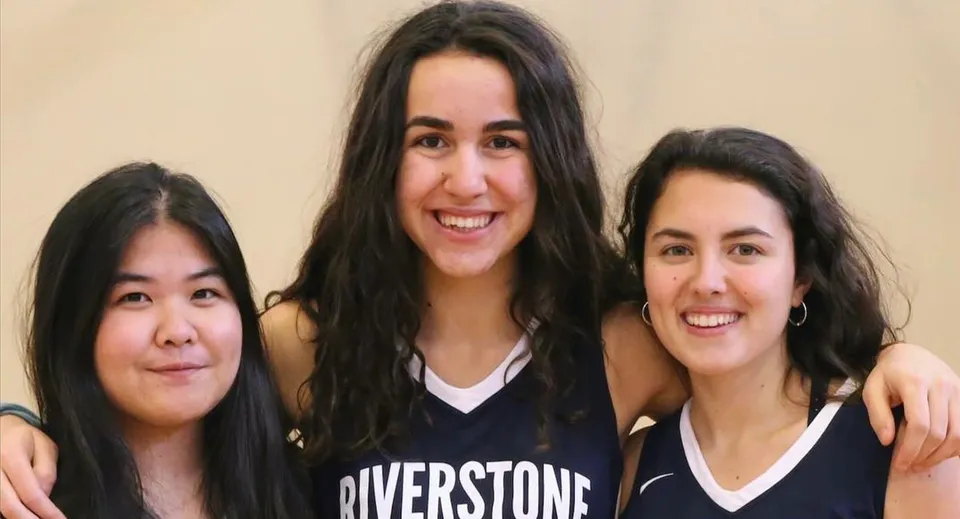 Tre studentesse con i capelli scuri sorridono e posano insieme in un ambiente rilassato nel campus della Riverstone International School.
