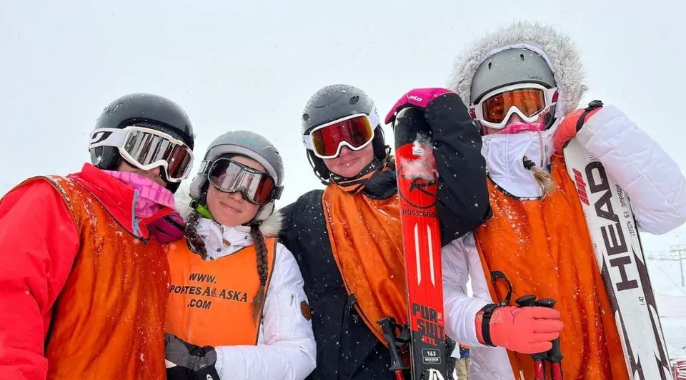 Un gruppo di studenti della Laude Lady Elizabeth School in piedi con abbigliamento invernale colorato e attrezzatura da sci davanti a un paesaggio innevato.