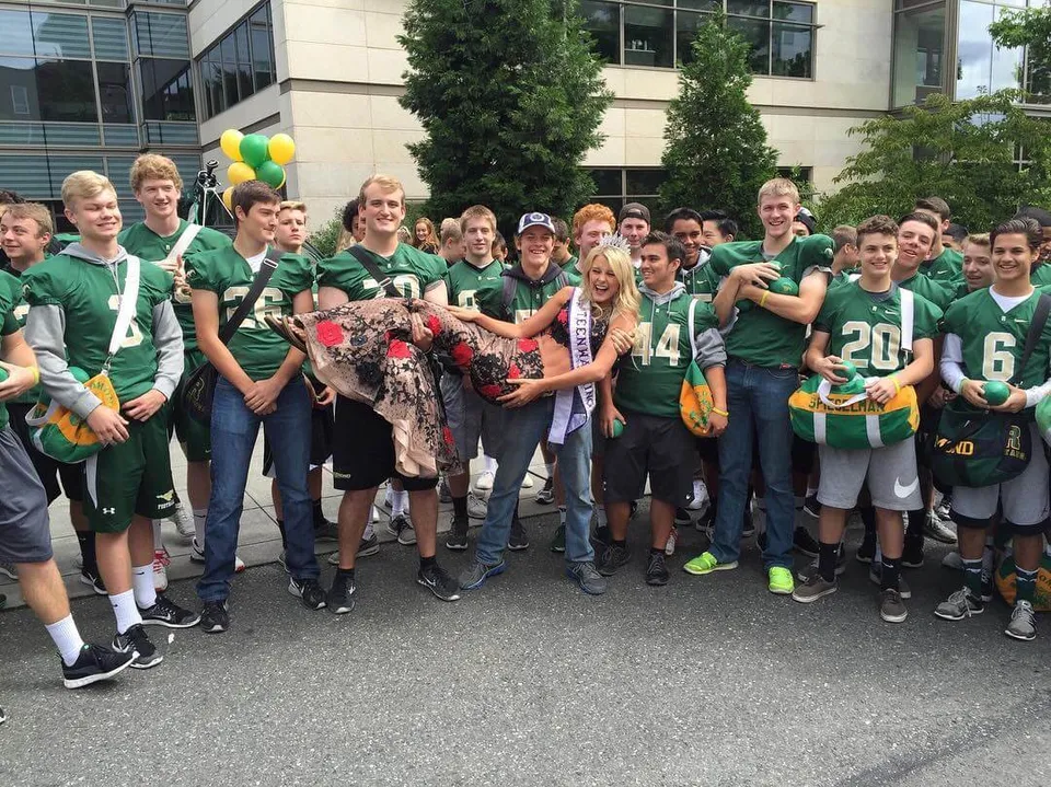 Studenti della Redmond High School si riuniscono davanti a un edificio in uniformi sportive verdi con palloncini.