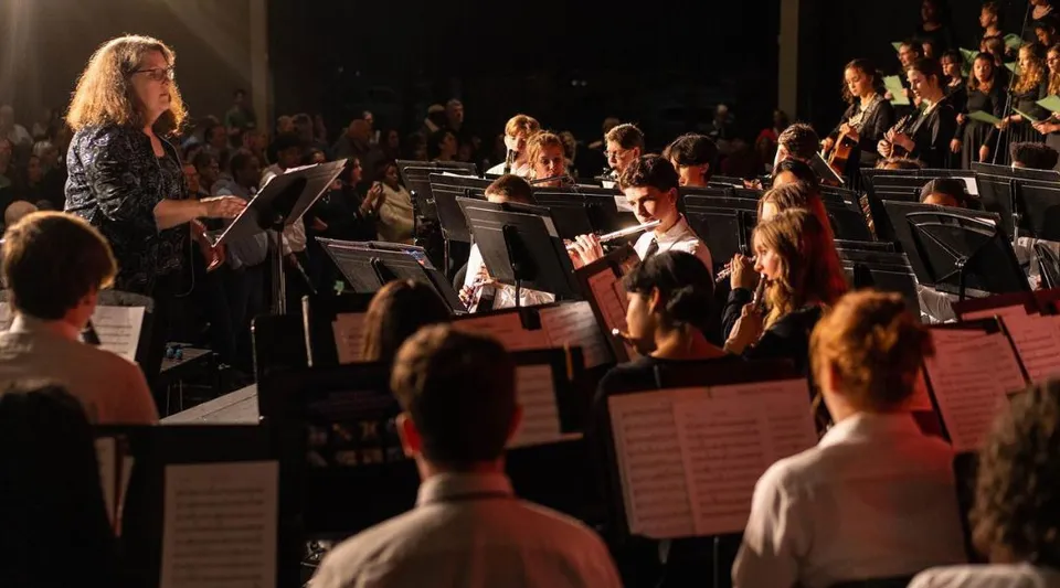 Un'ampia orchestra suona sul palco della Providence Christian Academy davanti a un pubblico visibile.