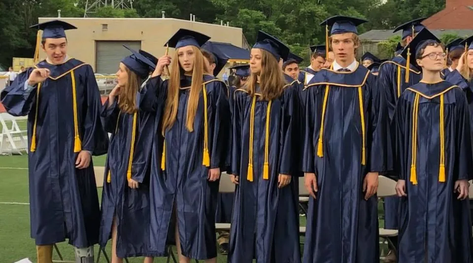 Un gruppo di diplomati in abito accademico si trova su un prato nel Mt. Lebanon School District.