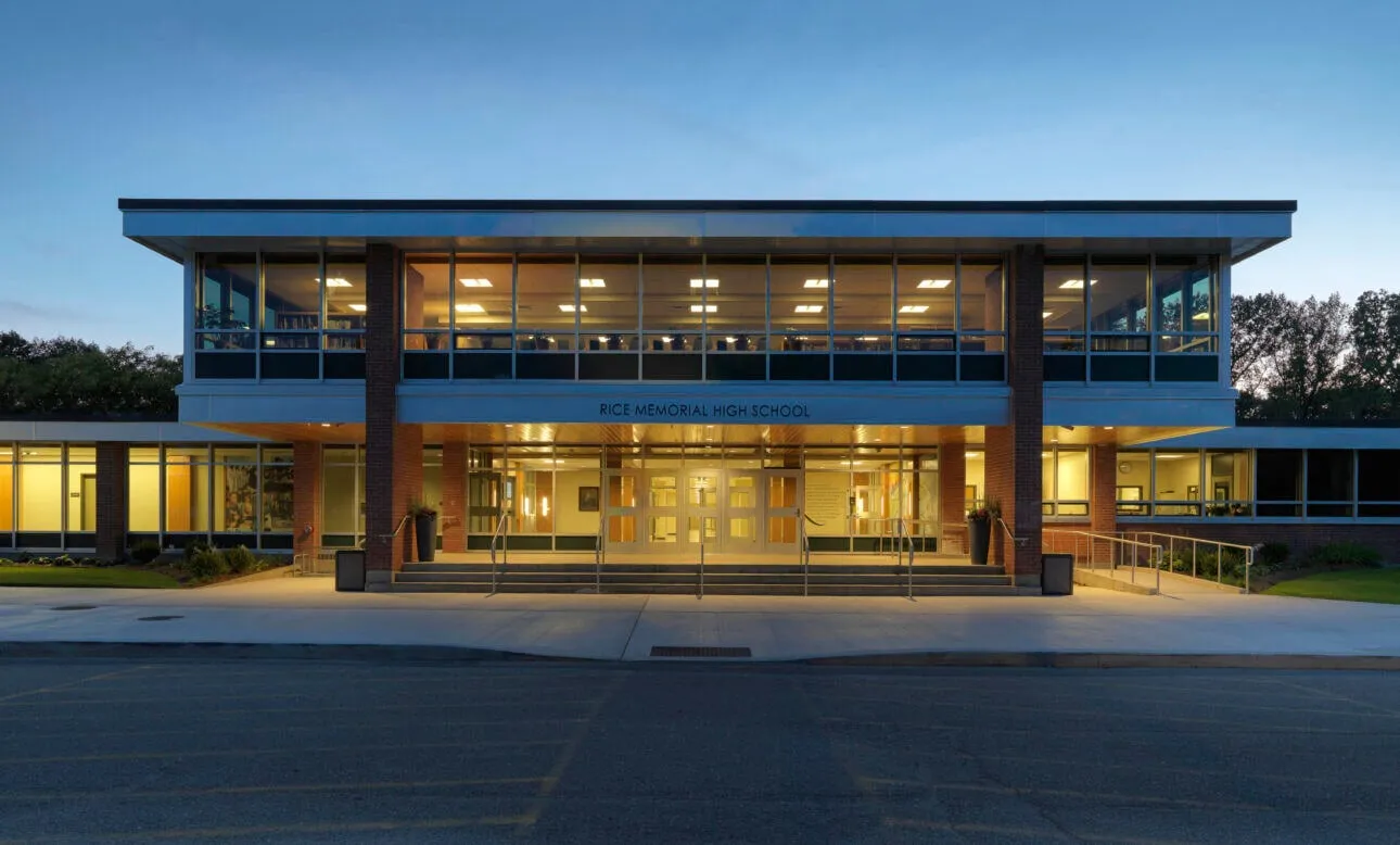 El moderno edificio de varios pisos de Rice Memorial High School con fachada de vidrio e interior iluminado.