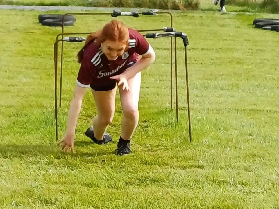 Una persona in abbigliamento sportivo si piega sul campo sportivo del Clonfert College davanti a un paesaggio erboso.