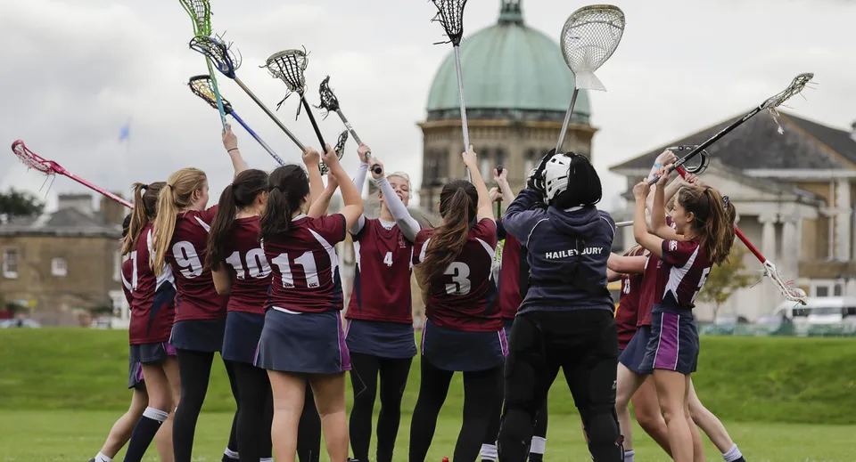 Un gruppo di giovani atlete con stecche da lacrosse posa davanti a un edificio storico nel campus della Haileybury School.