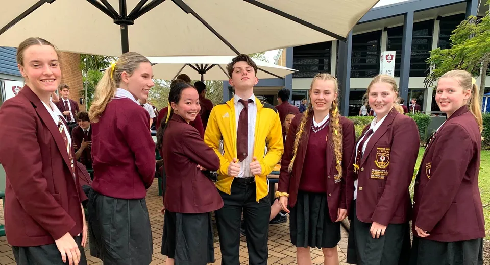 Un gruppo di studenti del St. Peters Lutheran College si trova all'aperto sotto un ombrellone.