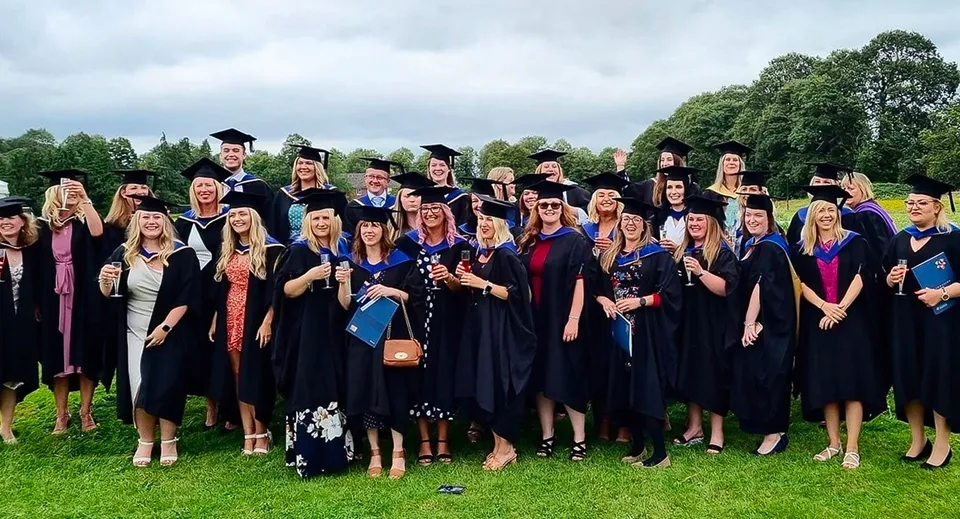 Un gruppo di diplomati si trova all'aperto nel verde del campus del Brockenhurst College in abito accademico.