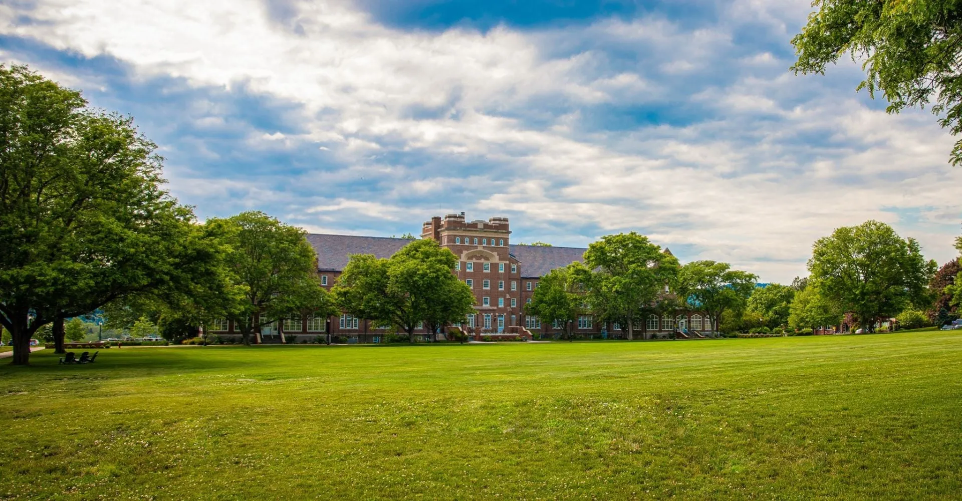 Il campus della Trinity-Pawling School mostra un grande prato verde davanti a edifici storici in mattoni sotto un cielo nuvoloso.