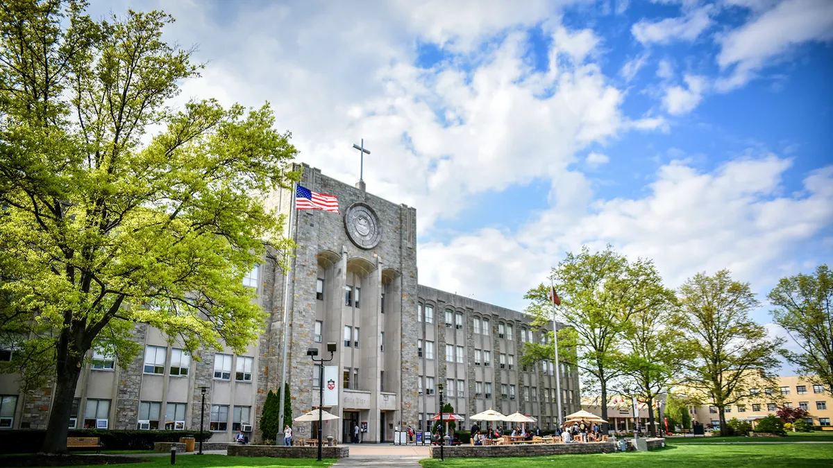 Edificio principale della St. John's University con torre dell'orologio e bandiera americana, circondato da alberi
