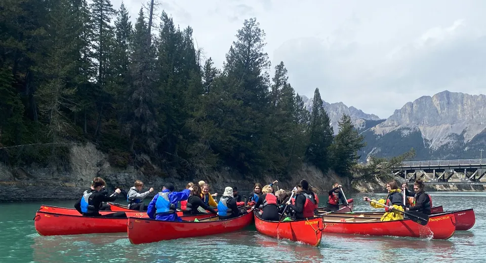 Studenti della Drumheller Valley in canoe rosse su un fiume circondato da alberi e montagne.
