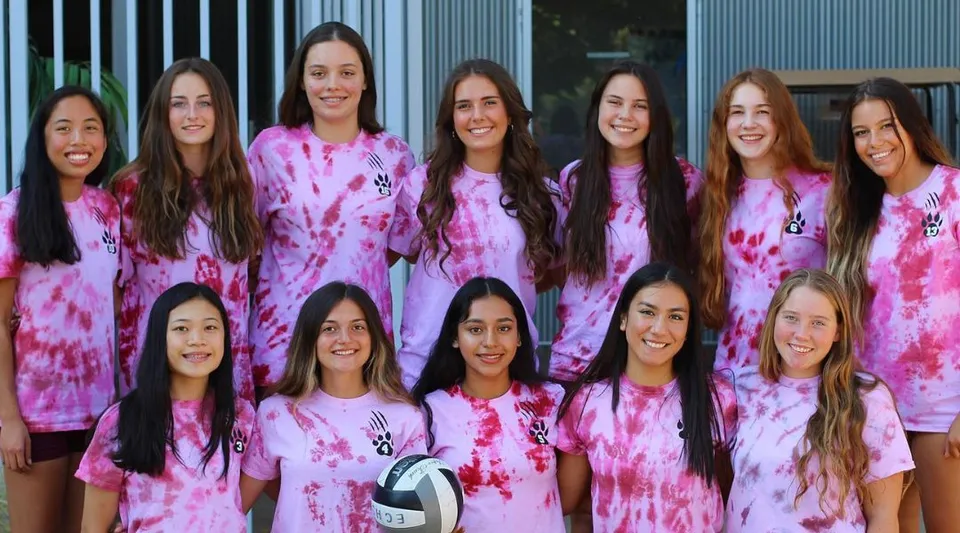 Un gruppo di studentesse della Escondido Charter High School è in piedi davanti a un edificio metallico grigio e indossa maglie tie-dye rosa.