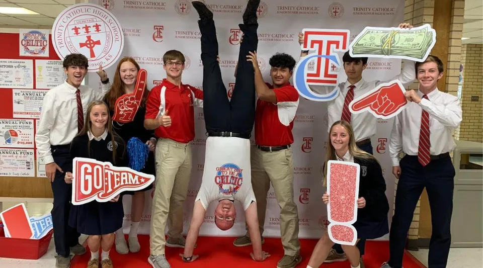 Un gruppo di studenti posa in abiti rossi e bianchi nel campus della Trinity Catholic Jr/Sr High School.