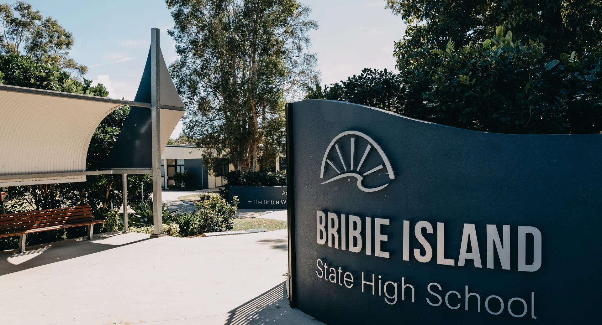 Si vede un cartello della Bribie Island State High School con un edificio e alberi sullo sfondo.