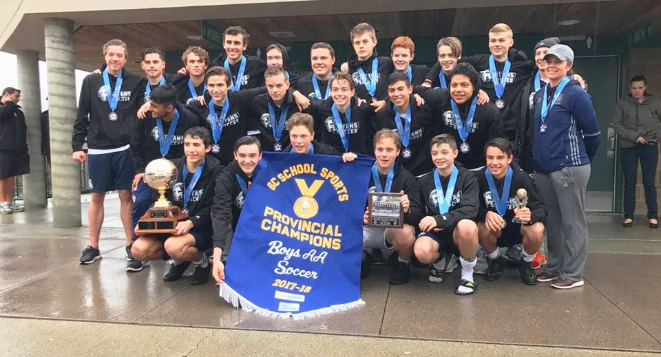 La squadra di calcio della Langley Fundamental Middle and Secondary School posa insieme a una coppa in una palestra al coperto.