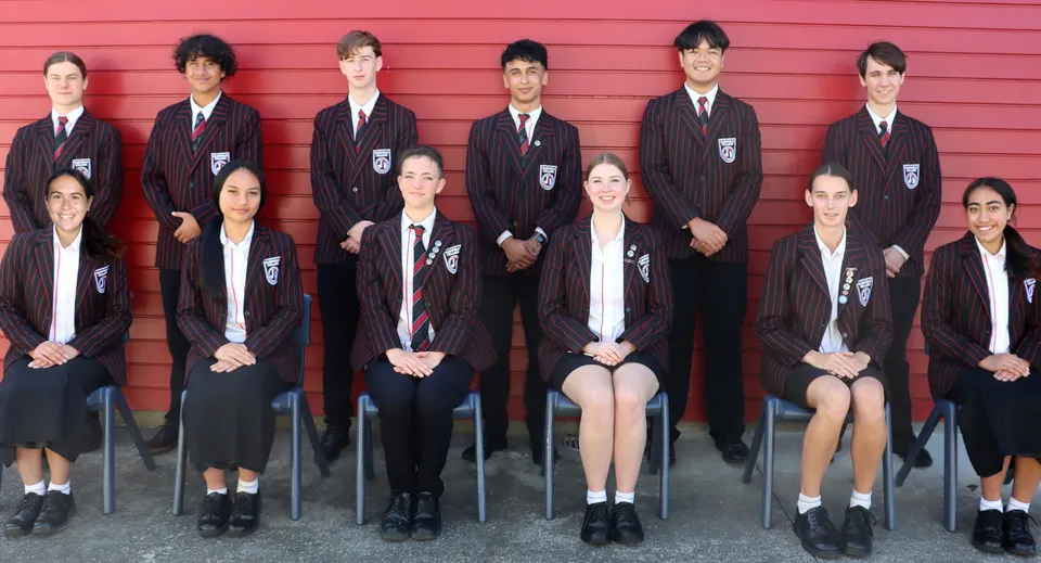 Un gruppo di studenti del Glenfield College è in piedi davanti a una parete di legno rossa.