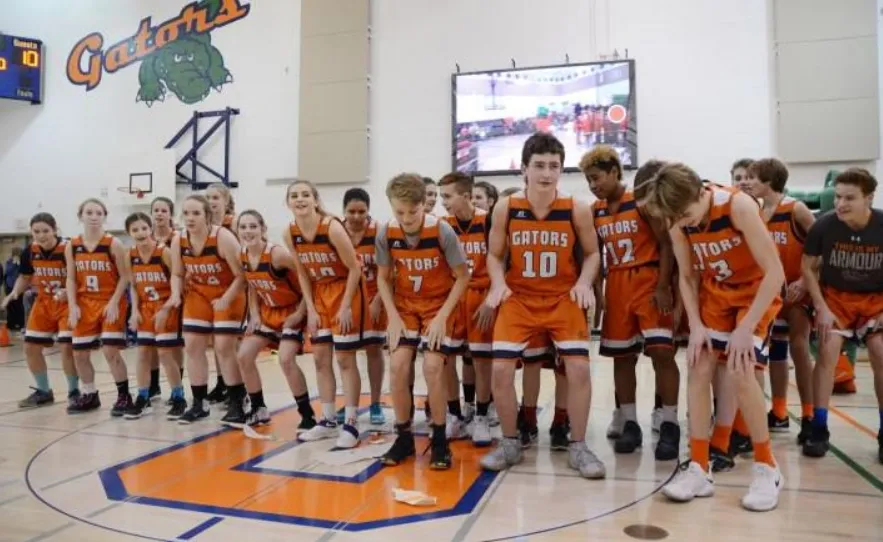 Un grupo de jóvenes jugadoras y jugadores de baloncesto de la Lethbridge School Division está junto en un gimnasio.