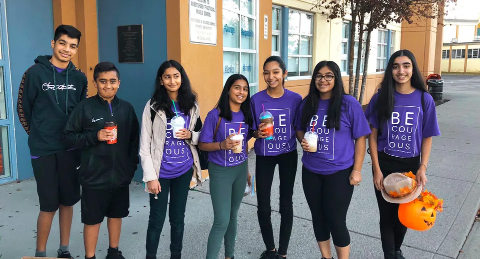 Un gruppo di studenti e studentesse davanti al vivace edificio colorato della Abbotsford Traditional Secondary School.