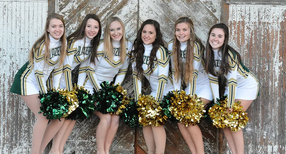 Un gruppo di cheerleader della Beckman Catholic School posa con pompon oro-verdi davanti a uno sfondo in legno invecchiato.