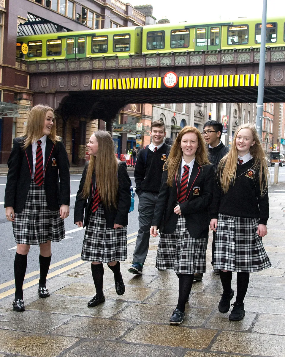 Studenti della CBS Westland Row in divisa si trovano in una strada con edifici storici sullo sfondo.