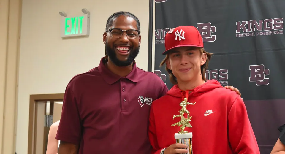 Un uomo con la barba e un ragazzo con un cappello rosso posano insieme durante un evento sportivo nel campus della Bethel Christian Schools.