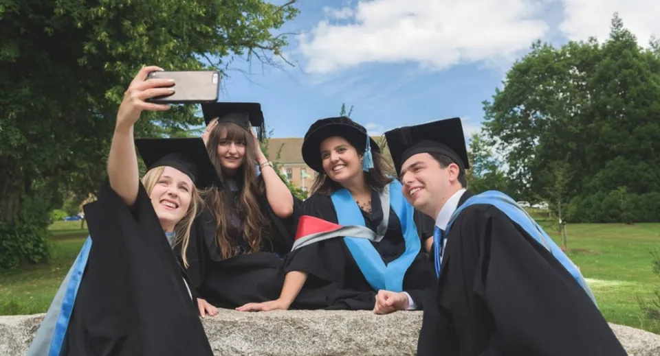 Quattro diplomati del Newstead College in toga accademica si scattano un selfie all'aperto.