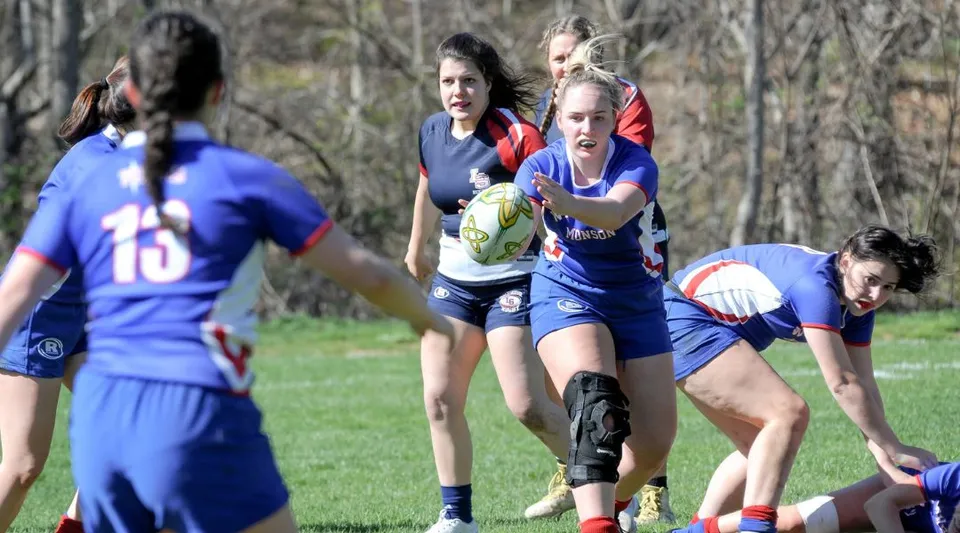 Giocatrici di rugby della Wilbraham & Monson Academy durante una partita su un campo d'erba con alberi sullo sfondo.